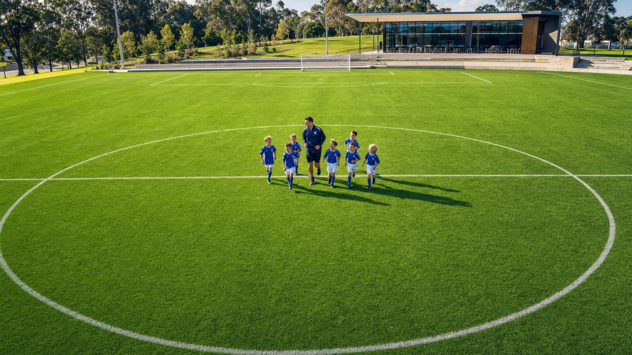A drone view of a huge, almost empty football pitch, with a small group of juniors and their coach jogging across the centre circle.